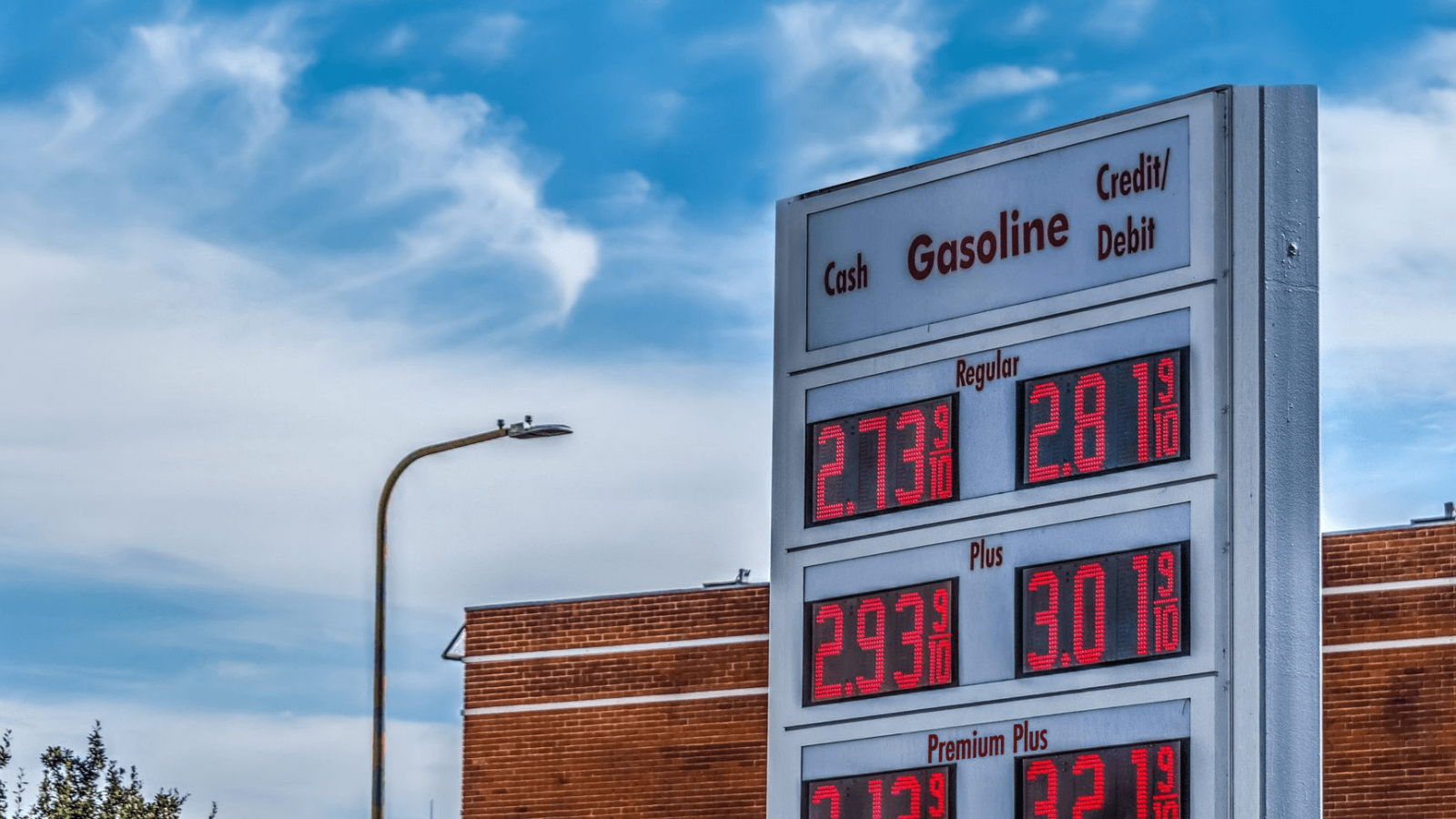 Gas station price sign under a clear blue sky displays different gasoline prices.